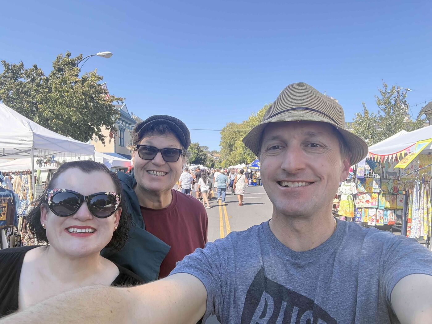 Justin Zollars with two friends at a street fair on First Street in Benicia, vendor booths lining the closed street behind them.