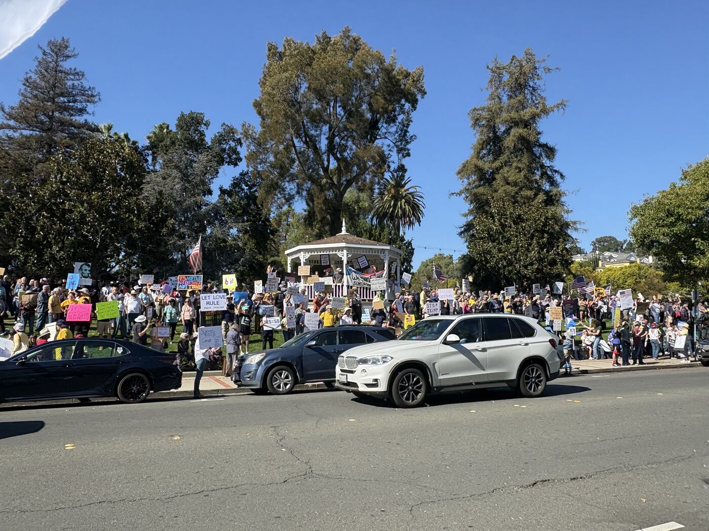 A large crowd of demonstrators with hand-made signs filling the lawn around the gazebo at Benicia City Park.
